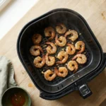 Seasoned shrimp in a single layer in an air fryer basket, curling and turning pink at the edges