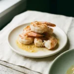 Close-up of finished shrimp on a cream plate with emulsified butter sauce pooling around the base