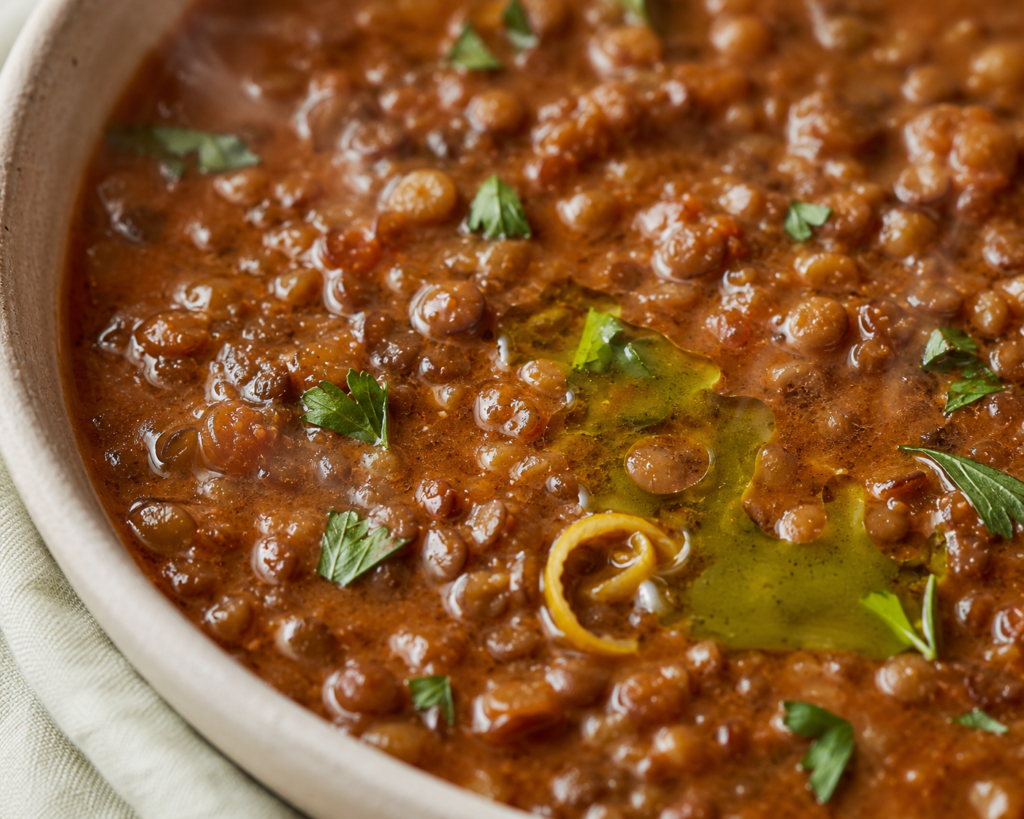Close view of Mediterranean lentil soup showing whole lentils, a swirl of olive oil, and torn parsley
