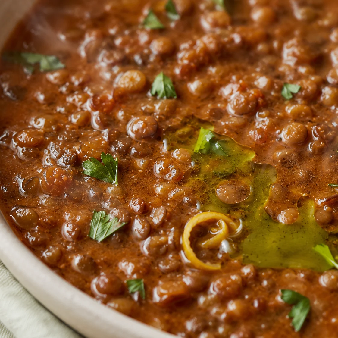 Close view of Mediterranean lentil soup showing whole lentils, a swirl of olive oil, and torn parsley