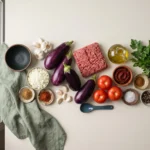 Raw eggplants, ground beef, tomatoes, onion, garlic, lemon, parsley, and spices for Mediterranean stuffed eggplant with ground beef