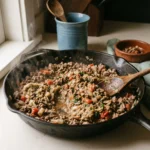 Ground beef, eggplant flesh, onion, and tomatoes being stirred in a skillet for stuffed eggplant