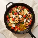Mediterranean shrimp skillet for two in a cast-iron pan with blistered tomatoes, spinach, olives, feta and lemon