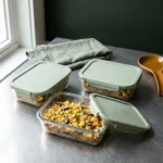 Three glass meal-prep containers packed with cooled cauliflower fried rice on a grey stone counter.