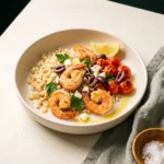 Keto Mediterranean shrimp with cauliflower rice in a cream bowl with blistered tomatoes, olives, feta and a lemon wedge