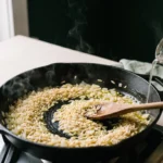 Dry orzo toasting with onion and garlic in an oiled skillet as broth is poured in