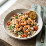 Mediterranean shrimp couscous in a white bowl with charred shrimp, blistered tomatoes, olives, feta and a grilled lemon half
