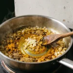 Ground turmeric, cumin and coriander half stirred into hot olive oil with softened onion and garlic in a steel saucepan