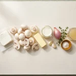 Raw white mushrooms, cream cheese, butter, heavy cream, shallot, garlic and thyme laid out on a pale board