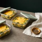 Three glass meal-prep containers of spaghetti squash and broccoli bake with sage lids on a stone counter