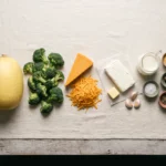Raw spaghetti squash, broccoli florets, block cheddar, cream cheese and heavy cream laid out on linen