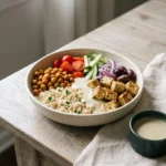 Vegan Mediterranean rice bowl with crispy chickpeas, roasted tofu, tomatoes, olives and tahini sauce