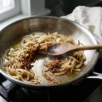 Sliced onions part-way through caramelizing in a stainless skillet with a wooden spoon mid-stir