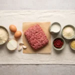 Raw ingredients for keto meatloaf: ground beef, almond flour, eggs, parmesan, cream, tomato paste, thyme
