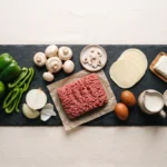 Raw ground beef, green bell pepper, onion, mushrooms, provolone slices and cream cheese on a slate board
