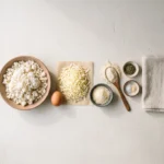 Frozen riced cauliflower, egg, mozzarella, Parmesan, almond flour and dried herbs laid out on pale plaster