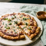 High protein chicken crust pizza sliced on a pale ceramic board, melted mozzarella and torn basil on top