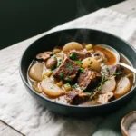 Keto beef stew with radishes in a dark bowl, braised beef, pale radish halves and mushrooms in a glossy broth