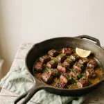 Keto cowboy butter steak bites in a cast iron skillet with melted herb butter, parsley and a lemon wedge