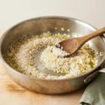 Rice grains toasting with softened onion and garlic in olive oil in a wide stainless saute pan