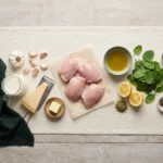 Raw chicken thighs, garlic, cream, Parmesan, butter, spinach and lemon laid out on a linen runner