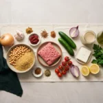 Raw ingredients for Mediterranean beef bowls: ground beef, dry bulgur, chickpeas, cucumbers, tomatoes, tahini, feta and lemon