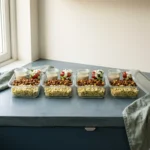 Four glass meal prep containers packed with lemon bulgur, spiced beef and chickpeas, salad and tahini sauce
