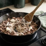 Stirring melted cream cheese into browned ground beef for keto ground beef casserole in a skillet