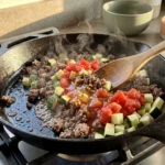Ground beef and diced zucchini being stirred together in a skillet