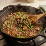 Ground beef and mushrooms simmering in Worcestershire pan sauce, mid-reduction in a skillet
