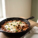 Close-up of a keto italian ground beef skillet in a cast iron pan with melted mozzarella and basil