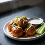 Keto buffalo chicken meatballs coated in buffalo butter sauce on a white plate with ranch and celery