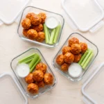 Buffalo chicken meatballs portioned into glass meal-prep containers with celery and ranch