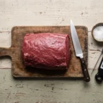 Raw trimmed beef and kosher salt for carnivore beef jerky before slicing