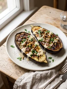Roasted eggplant with lemon tahini, toasted pine nuts, and parsley on a ceramic plate
