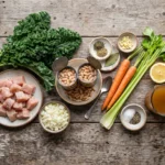 Raw ingredients for high protein white bean chicken kale soup laid out on a wood board