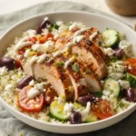 Plated keto Mediterranean cauliflower rice bowl with chicken, vegetables, feta, olives, and yogurt sauce
