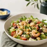 Close-up of no cook Mediterranean shrimp salad with chilled shrimp, chickpeas, arugula, olives, feta, and lemon