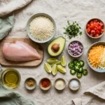 Raw ingredients for a chicken burrito bowl under 500 calories, including chicken breast, cauliflower rice, avocado, and lime