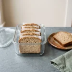 Cooled slices of keto bread stacked with parchment between them in a glass storage container