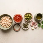 Drained butter beans, crushed tomatoes, green olives, capers, garlic and olive oil laid out raw